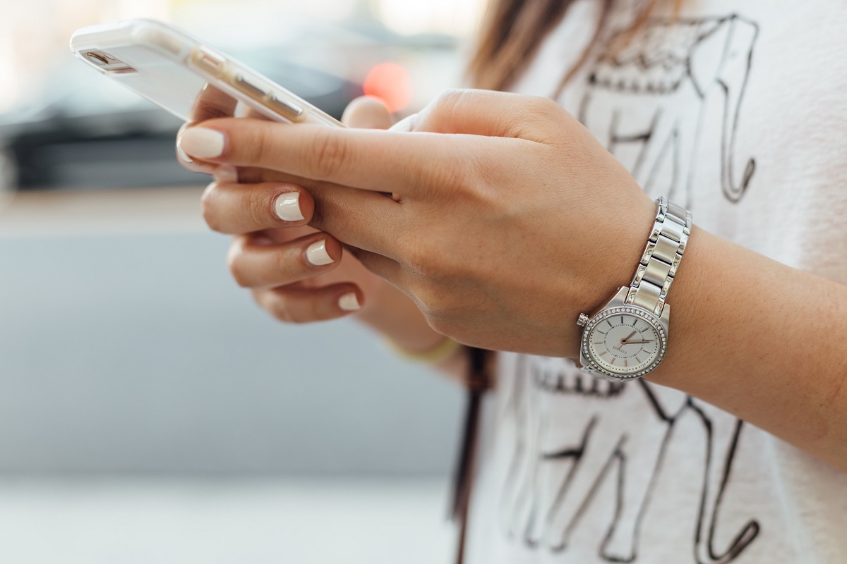 Mulher em celular na mão enquanto digita algo no smartphone e relógio prateado no seu punho.