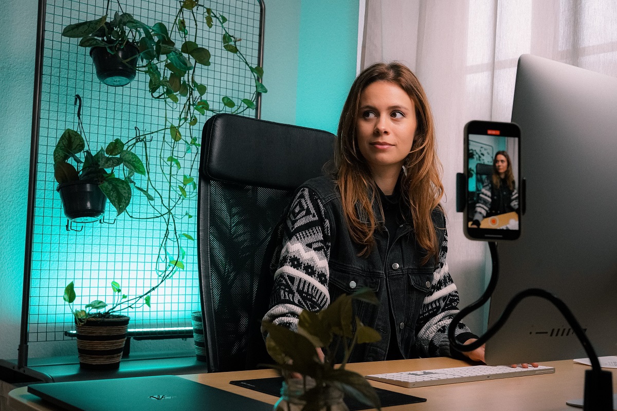 mulher sentada, gravando um vídeo com o celular apoiado em um tripé a sua frente