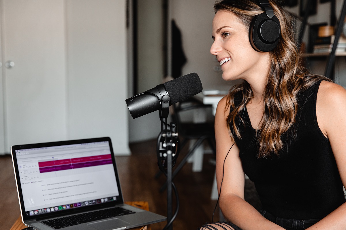 mulher sorrindo, com um headset e gravando áudio com a ajuda de um laptop e microfone