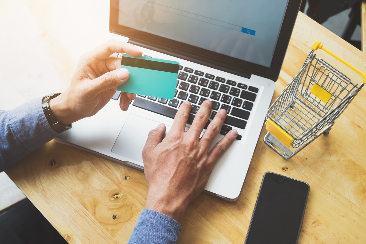 mão masculina segurando um cartão de crédito enquanto digita em um laptop