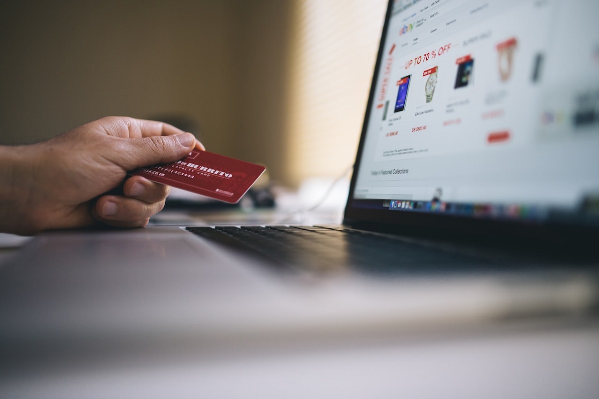 mão feminina segurando um cartão de crédito vermelho de frente para um laptop