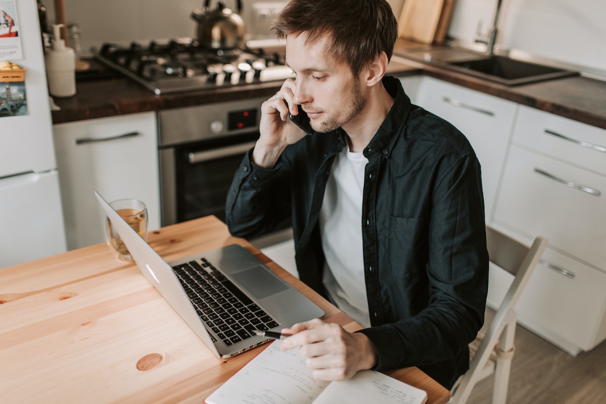 homem sentado, usando o celular e o laptop ao mesmo tempo