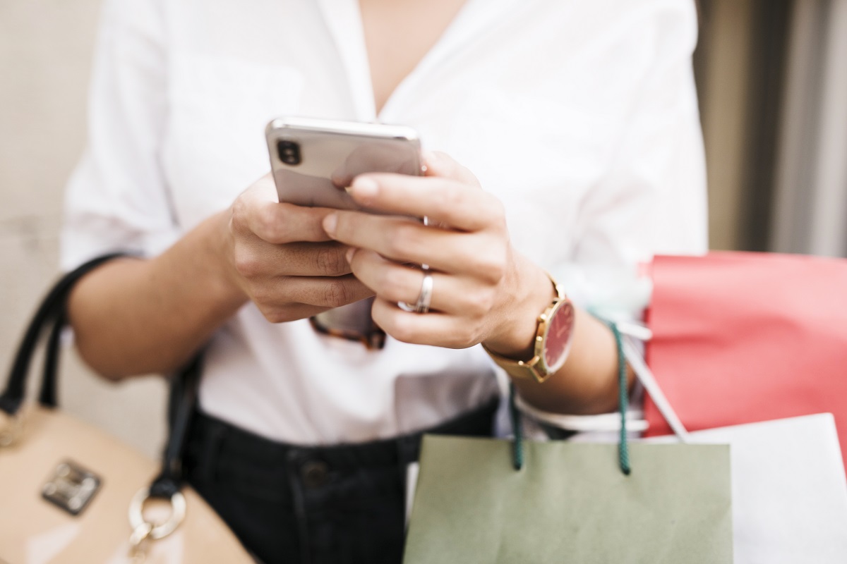 mulher com os braços com sacolas de compras e mexendo no celular