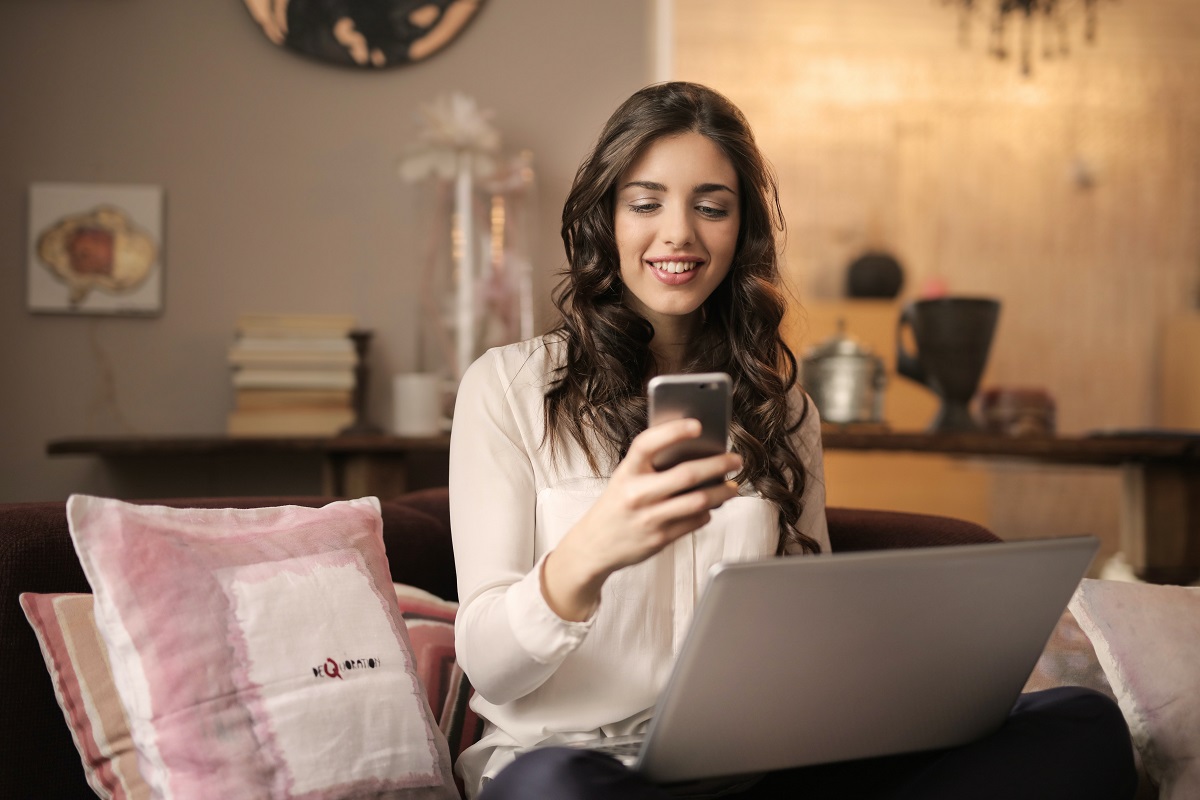 Mobile marketing: A imagem mostra uma mulher utilizando de um smartphone e de um computador ao mesmo tempo. 